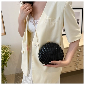 Close-up of black shell-shaped evening clutch with glossy texture and gold chain strap