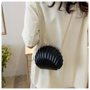 Elegant black shell-shaped clutch bag with golden chain worn over an ivory blazer
