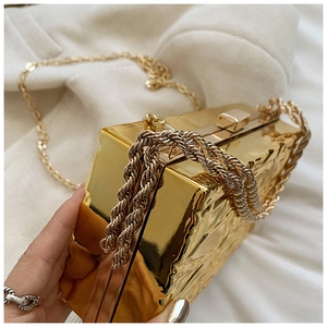 Dettaglio di borsa a mano dorata con texture martellata e tracolla a catena