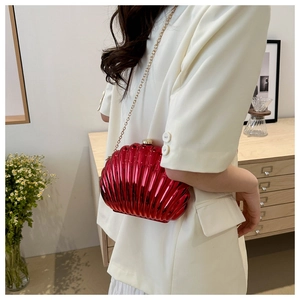 Detail of red metallic shell evening bag with golden chain strap on a model
