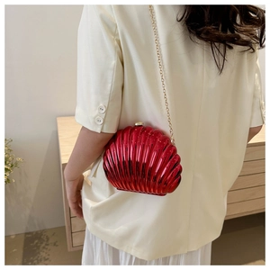 Detail of red metallic shell-shaped clutch bag with golden chain on model's shoulder