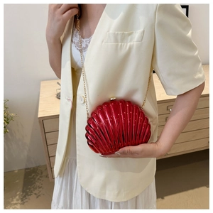 Detail of red shell-shaped evening bag with gold chain strap on white outfit