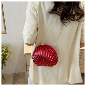 Detail of red candy-colored shell clutch bag with gold chain strap on a model
