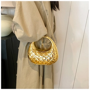 Detail of gold quilted acrylic box bag with metal chain on model wearing khaki trench coat