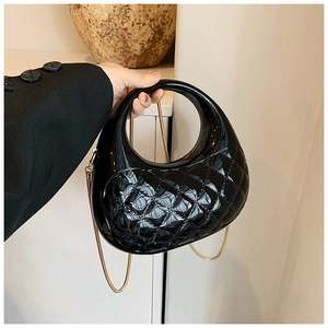Detail of black diamond-quilted acrylic box bag with gold chain and circular handle
