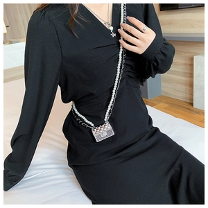 Detail of silver quilted mini bag with pearl chain on black dress worn by model