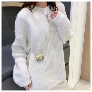 Detail of a mini quilted gold crossbody bag with a pearl strap on a white knit sweater