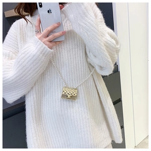 Detail of a mini gold quilted bag with pearl chain shown on white knit sweater