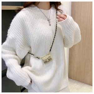 Detail of a gold quilted mini bag with pearl strap on a white knit sweater