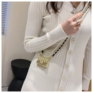 Detail of a mini gold quilted bag with pearl chain strap worn on a white dress