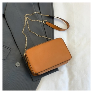 Flat lay of a brown camera crossbody bag on a grey blazer with golden chain strap