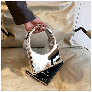 Close-up of a silver mirror finish hard-shell handbag with circular handles on a sofa