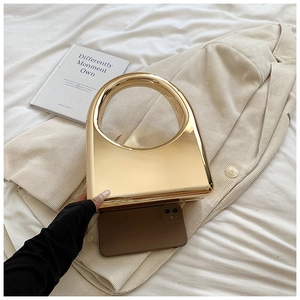 Detail of a gold metallic hard shell mini bag with a round handle on a beige blazer