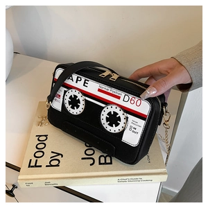 Macro detail of retro cassette tape shaped crossbody bag resting on a pile of books