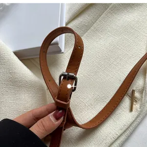 Detailed close-up of brown faux leather shoulder strap with silver metal buckle and holes