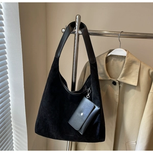 Detail of black suede hobo bag with leather pouch hanging on a steel display stand