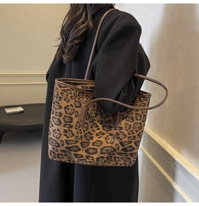 Detail of leopard print tote bag with brown leather trim and zipper closure worn by model