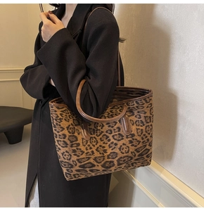 Detail of a large leopard print tote bag with brown leather straps on a black coat