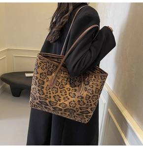 Detail of a large leopard print tote bag with brown leather straps worn by a model