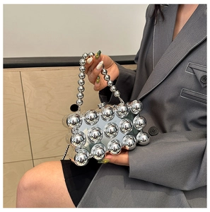 Detail of silver metallic evening bag featuring glossy spherical texture and beaded handle