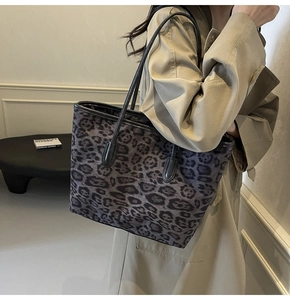 Detail of large leopard print tote bag with black straps worn over a beige trench coat
