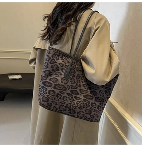 Detail view of large leopard print tote bag with black leather straps on a khaki coat