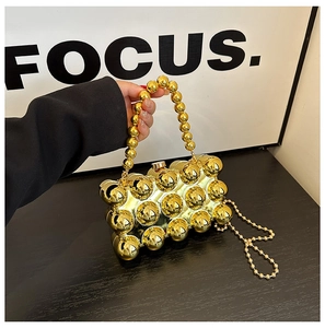 Detail of gold hard-shell evening bag with spherical texture and metallic beaded handle