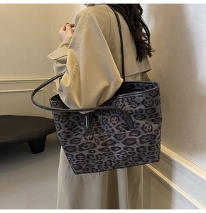Large leopard print tote bag with black handles shown on model shoulder in a French interior