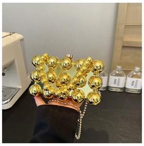 Close-up of golden evening clutch with 3D metal sphere texture and fine chain strap