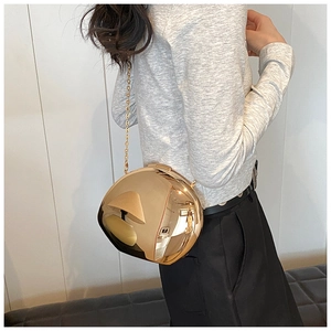 Dettaglio di una borsa a sfera dorata in acrilico a specchio con sottile tracolla a catena