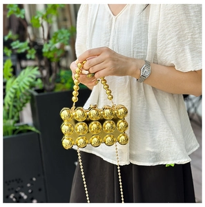 Close-up of gold metal evening clutch with 3D bead texture and sphere handle link