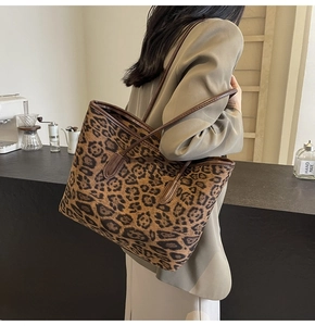 Close-up of a large leopard print tote bag with brown straps worn by a model in a cafe