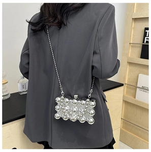 Detail of silver metallic sphere clutch bag with a slim bead chain strap worn by a model