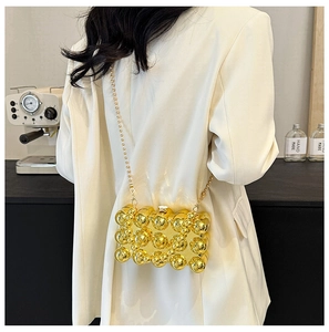 Golden spherical evening bag with metal beads shown worn over a white blazer