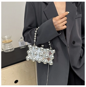Detail of silver metallic egg-shaped bag with bubble texture and chain strap worn by model