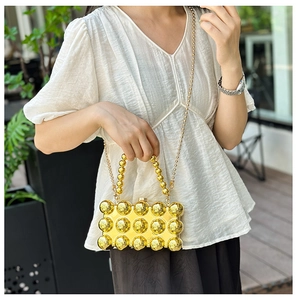 Detail view of a gold evening box bag with 3D spherical studs and a bead chain strap