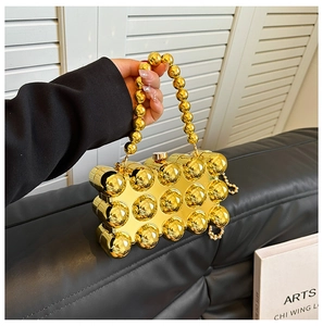 Detail of gold metallic sphere evening bag featuring round bead handle and chain strap