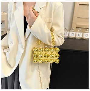 Detail of a structured gold evening clutch with metallic globes and delicate chain strap