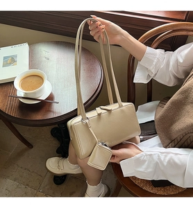 Detail view of cream rectangle underarm bag with matching mini pouch on a cafe table