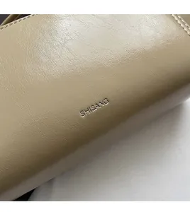 Detailed macro shot of glossy beige leather texture and silver logo on shoulder bag