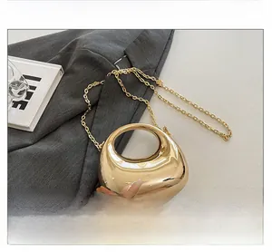 Detail of a gold metallic bean-shaped evening bag with a shiny mirror finish and chain