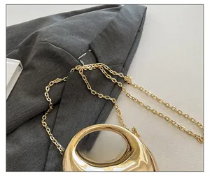 Detail of gold crescent handbag featuring polished metal handle and delicate chain strap