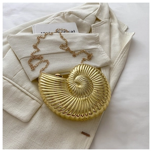 Détail d'une pochette coquillage dorée sur un blazer beige avec une bandoulière en chaîne