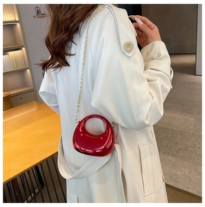 Detail of red metallic crescent mini bag with gold chain strap worn over white coat
