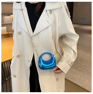 Blue mini moon crossbody bag with gold chain strap shown on a white coat outfit