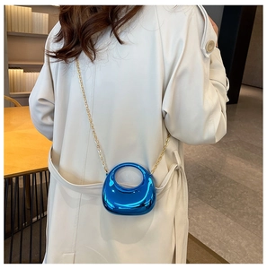 Close-up of mini electric blue metallic crossbody bag with gold chain strap on white coat