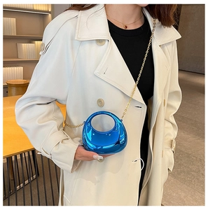 Close-up of electric blue crescent mini bag with gold chain strap on white coat