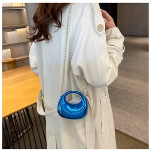 Detail of blue mirrored semi-circle clutch bag with gold chain strap on a white coat