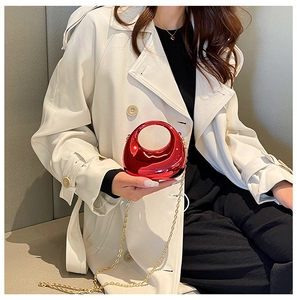 Mini metallic red evening bag with golden chain strap shown on a white trench coat
