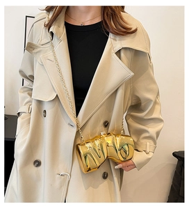 Detailed view of an irregular gold evening clutch with a lava texture on a beige trench coat